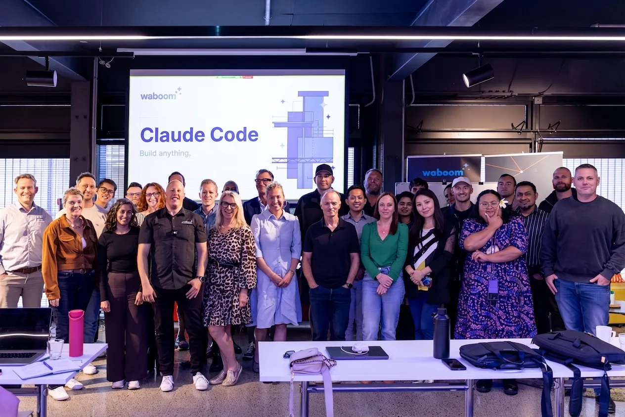 Attendees at a Waboom AI Claude Code workshop in New Zealand standing in front of a Claude Code slide